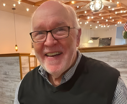 Jerry Eddy, man with a dark sweater vest and black and white shirt on under it with black framed glasses.