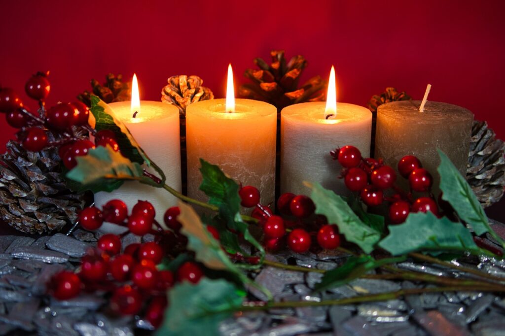 Advent candles lit with green holey, red berries and bine cones.