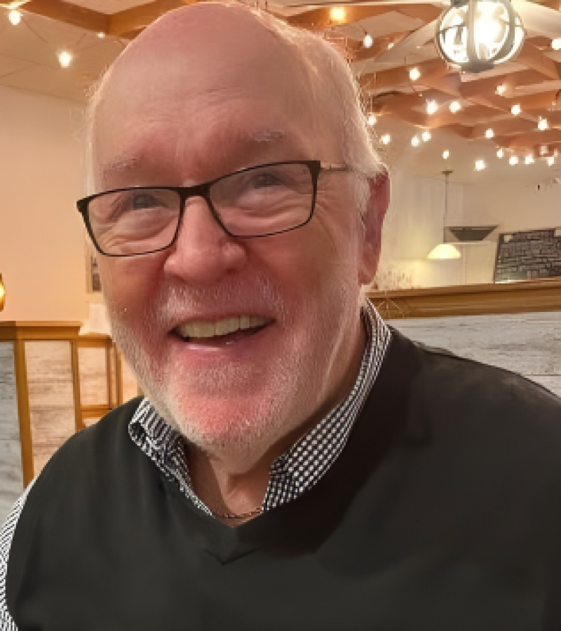 Jerry Eddy, man with a dark sweater vest and black and white shirt on under it with black framed glasses.