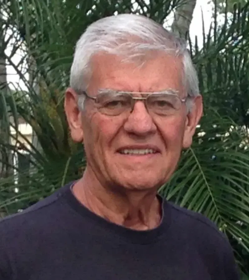 Roger Brewer smiling man with dark blue shirt and a fern tree behind him